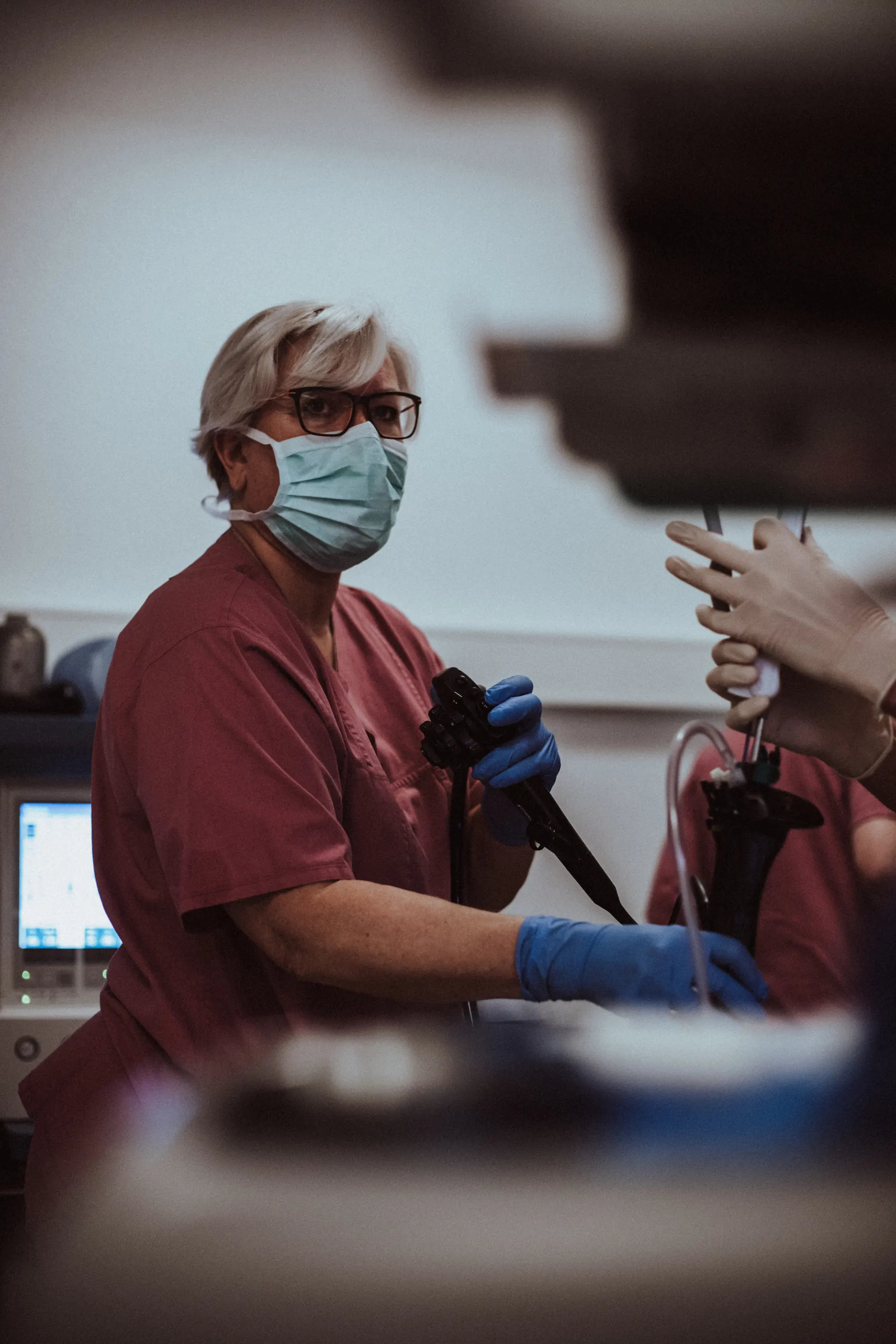 Collaboratrice con mascherina e guanti che tiene un endoscopio in sala visite